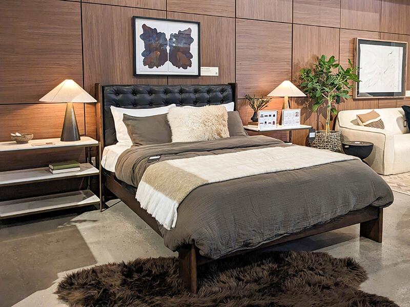 A black leather bed and metal nightstands against a deep brown panelled wall